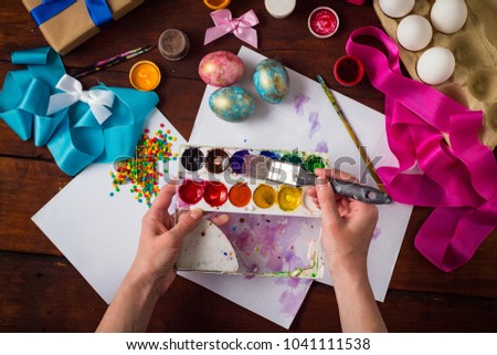 Preprimary painting of Easter Eggs, Brushes, Paints, Eggs, Sweets, Ribbons on the Dark Wooden Table. The concept of Easter. Flat lay, top view.