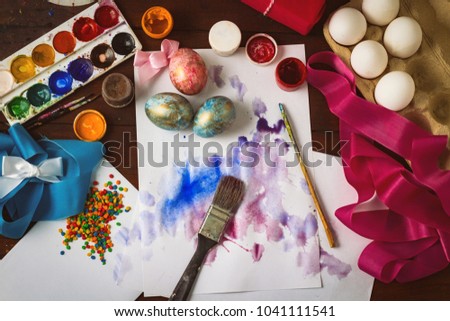 Preprimary painting of Easter Eggs, Brushes, Paints, Eggs, Sweets, Ribbons on the Dark Wooden Table. The concept of Easter. Flat lay, top view.