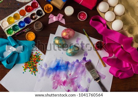 Preprimary painting of Easter Eggs, Brushes, Paints, Eggs, Sweets, Ribbons on the Dark Wooden Table. The concept of Easter. Flat lay, top view.