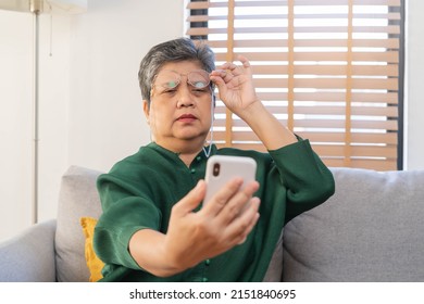 Presbyopia, Hyperopia Mature Asian Woman Holding Eyeglasses Having Problem With Vision Problem Trying To Read Text On Mobile, Eye Disease Of Old Elderly Sitting On Couch. Poor Eyesight, Health Care.