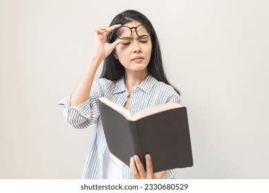 Presbyopia, hyperopia middle aged asian woman holding eyeglasses problem with vision blurred, female stare trying to read text on book on white background, eye disease of old, eyesight farsightedness
