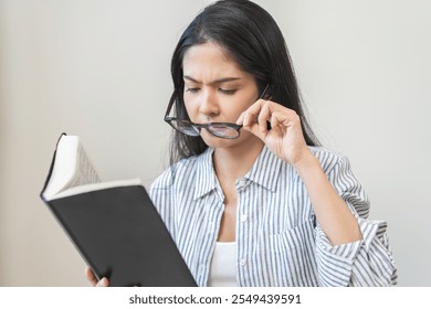 Presbyopia, hyperopia middle aged asian woman holding eyeglasses problem with vision blurred, female stare trying to read text on book at home, eye disease of old, eyesight farsightedness, health care