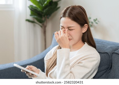 Presbyopia, Hyperopia middle aged asian woman hand rubbing her eye with vision blurred ,girl trying to read text message from smart mobile phone screen, eye disease of old, eyesight farsightedness.
