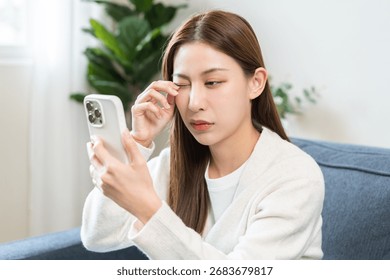 Presbyopia, Hyperopia middle aged asian woman hand rubbing her eye with vision blurred ,girl trying to read text message from smart mobile phone screen, eye disease of old, eyesight farsightedness.