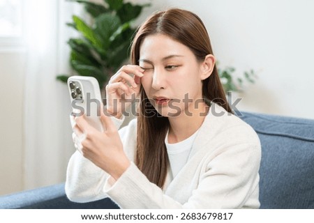 Presbyopia, Hyperopia middle aged asian woman hand rubbing her eye with vision blurred ,girl trying to read text message from smart mobile phone screen, eye disease of old, eyesight farsightedness.