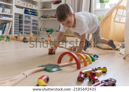 Preschool baby boy playing wooden Montessori materials rainbow arch railways at childish room. Playthings storage cupboard arrangement organizing. Male kid with natural eco friendly toys at home