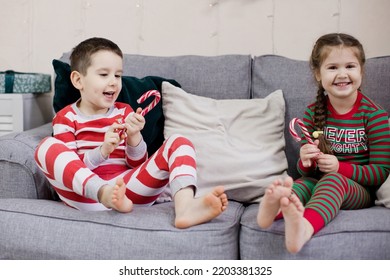 Preschool Boy And Girl In Christmas Pyjamas Sitting On A Grey Sofa