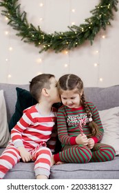 Preschool Boy And Girl In Christmas Pyjamas Sitting On A Grey Sofa