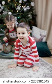 Preschool Boy And Girl In Christmas Pyjamas Sitting Near Christmas Tree