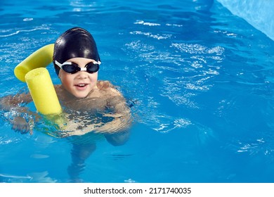 Preschool Boy Learning To Swim In Pool With Foam Noodle