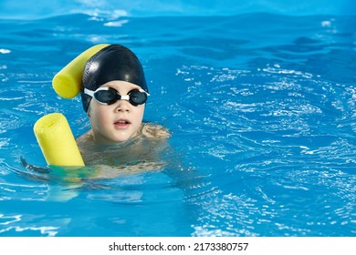 Preschool Boy Learning To Swim In Pool With Foam Noodle