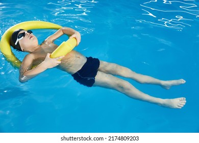 Preschool Boy Learning To Swim In Pool With Foam Noodle