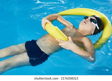 Preschool Boy Learning To Swim In Pool With Foam Noodle