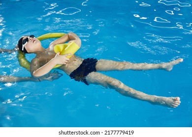 Preschool Boy Learning To Swim In Pool With Foam Noodle