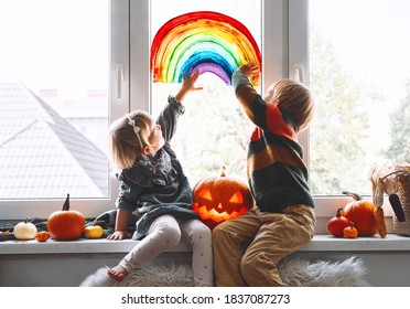 Preschool Children On Background Of Painting Rainbow On Window.  Family Preparing For Celebrating Halloween During Quarantine Pandemic Coronavirus Covid-19 At Home. Kids Leisure Activities Indoors.