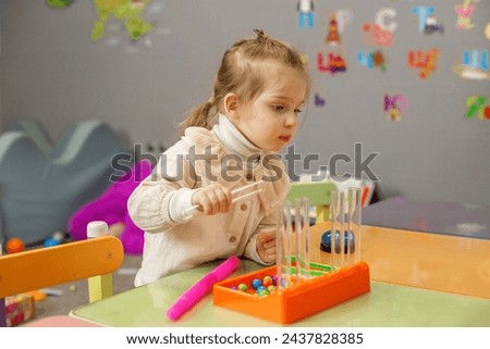 Preschool girl deeply focused on bead sorting task, developing cognitive and motor skills in an educational setting.