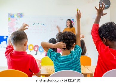 Preschool kid raise arm up to answer teacher question on whiteboard in classroom,Kindergarten education concept