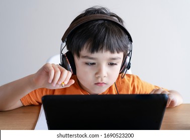 Preschool kid using tablet for his homework,Child wearing head phone doing homework by using digital tablet searching information on internet,Home schooling education concept,Social Distancing