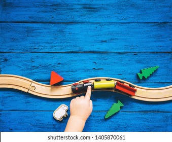 Preschool or kindergarten background with toys. Child's hands playing with wooden toy train set and railway on blue table. Kids dream, travel concept. Top view, flat lay, copy space.