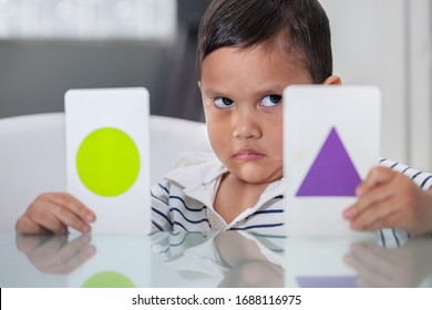 A Preschool Student With Upset Facial Expression Holding Up Two Flash Cards, To Express Children With Learning Dissabilities In Critical Areas Of Child Development.