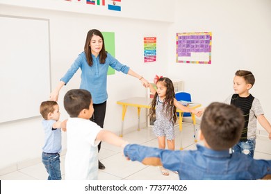 Preschool teacher holding hands with her students and making a circle in the classroom