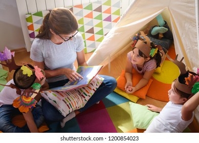 Preschool Teacher Reading A Story To Children At Kindergarten. Mother Reading To The Children.