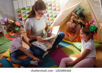 Preschool Teacher Reading A Story To Children At Kindergarten. Mother Reading To The Children.