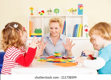 Preschool: Young Smiling Teacher Discussing With Group Of Children. Learning And Having Fun. Selective Focus To Teacher Talking.