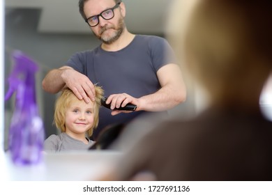 Preschooler Boy Gets Haircut At Home During Quarantine. Father Cuts His Son's Bangs With Hair Clipper. Reflection In Mirror. Hair Cutting For Kids By Parents While Hairdressers Closed.