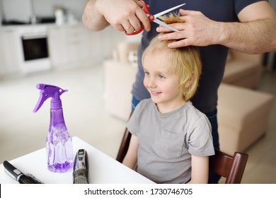 Preschooler Boy Gets Haircut At Home During Quarantine. Father Cuts His Son's Bangs With Scissors And Comb. Hair Cutting For Kids By Parents While Hairdressers Closed.