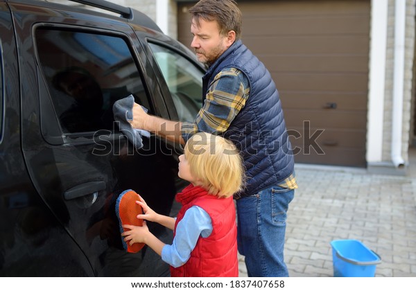 Preschooler boy helping his father washing\
family car. Little dad helper. Family with children spends time\
together in the\
backyard