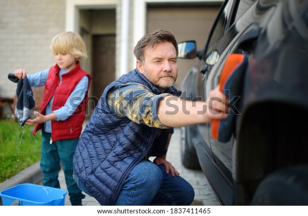 Preschooler boy helping his father washing\
family car. Little dad helper. Family with children spends time\
together in the\
backyard