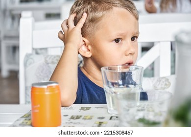 Preschooler Boy Sits In Restaurant Waiting For Order To Start Eating. Fair-haired Child Looks With Bored Expression Sitting At Wooden Table