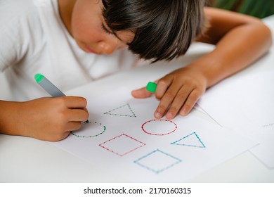 Preschooler boy sitting at the desk  drawing shapes 