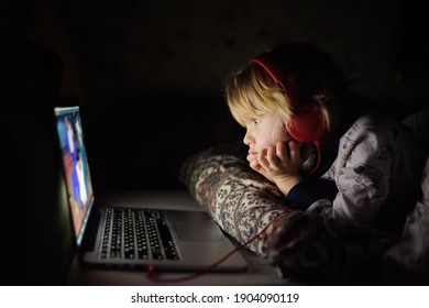 Preschooler boy is watching cartoon movie by laptop before sleeping in bed or early in the morning right after waking up. Overuse and addiction kids from gadgets. Entertainments for kids