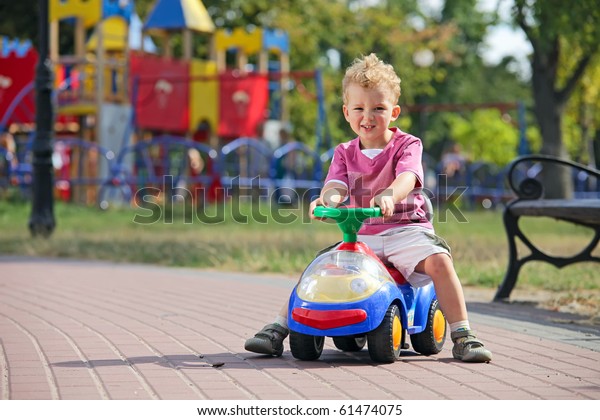 Preschooler driving\
his toy vehicle in the\
park
