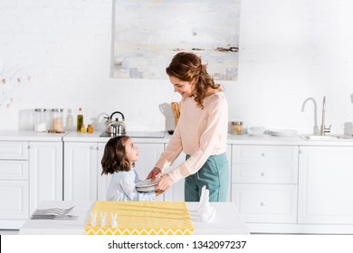 Preschooler Kid Helping Mother To Set Table In Kitchen