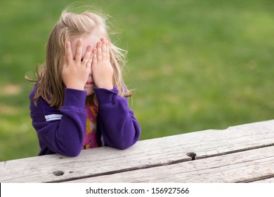 Preschooler Playing Game Of Hide And Sick. Right Now She Is Sitting On The Table Covering Her Eyes While Taking A Sneaky Peek.