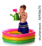 A preschooler pouring water from a plastic cup to a watering can while standing in a colorful kiddie pool.  Isolated on white.