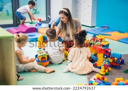preschoolers sitting on the floor surrounded plenty of toys and enjoying with their teacher, nursery. High quality photo