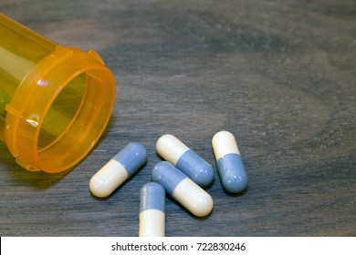 Prescription Drug Abuse Concept And Public Health Emergency. Blue And White Capsules On The Table Next To An Empty Prescription Bottle On A Dark Wood Background.
