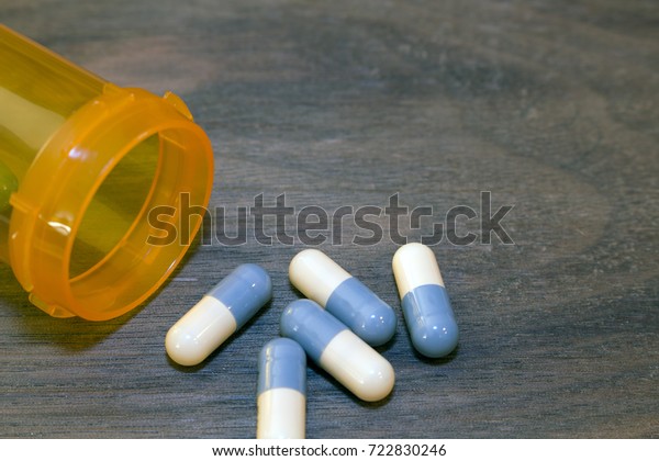処方薬乱用のコンセプトと公衆衛生上の緊急事態 暗い木の背景に空の処方箋ボトルの隣のテーブルに青と白のカプセル の写真素材 今すぐ編集