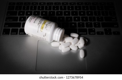 Prescription medication is strewn upon a laptop computer.