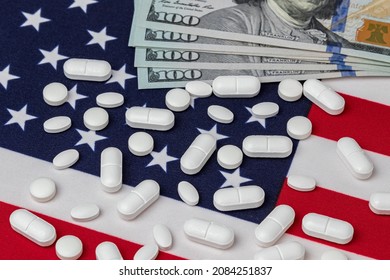 Prescription Medicine Pills And 100 Dollar Bills On American Flag. Pharmaceutical Industry, Imports And Exports, And Opiod Painkiller Addiction Costs Concept