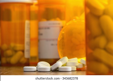 Prescription painkillers, oxycodone, spilling from a bottle on a table with other bottles out of focus.