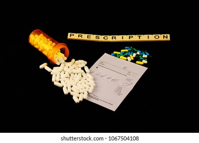 Prescription Spelled Out With Tiles Above Spilled White Pills Over A Prescription Pad And Colored Pills On A Black Background