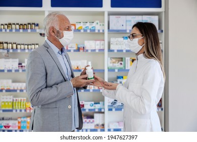 Prescriptions And Drugs For Therapy. An Older Man With Gray Hair In An Elegant Suit Talks To A Woman Pharmacist. Talk About Medical Therapy, A Protective Mask Against The Corona Virus. Drug Handover