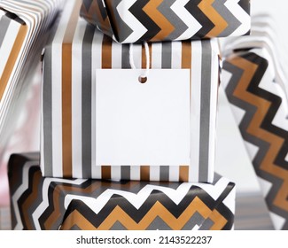 Present With Blank Square Gift Tag Close Up. Gift Boxes Wrapped In Striped And Chevron Geometric Paper. Christmas, New Year, Birthday, Anniversary Label Mockup