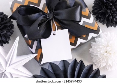 Present With Blank Square Gift Tag And Black Bow Close Up. Gift Boxes Wrapped In Striped And Chevron Geometric Paper Near Black And White Decor. Christmas, New Year, Birthday, Anniversary Label Mockup