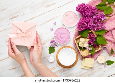 Present box in female hands. Spa and bath cosmetics with lilac flowers. Bath salt, soap, cream, oil, serum and towel rolls. Organic natural cosmetics. Beauty and relax healthcare. Gift certificate - Powered by Shutterstock